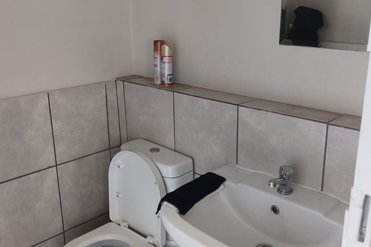 A compact bathroom featuring a pedestal basin, toilet, and neutral tiled finishes with a recessed wall mirror.