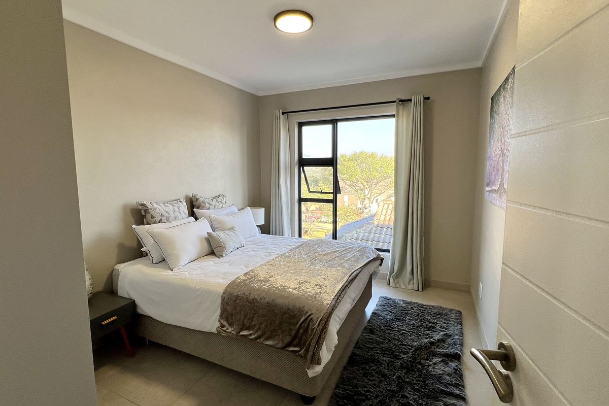 A well-maintained bedroom featuring neutral wall tones, tiled flooring, and a large window providing natural light and an exterior view.