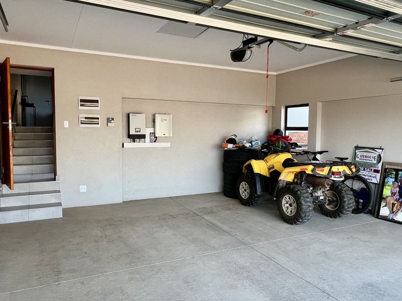Spacious double garage featuring concrete flooring, a sectional door, and a wall-mounted solar inverter and battery system with direct access to an internal staircase.