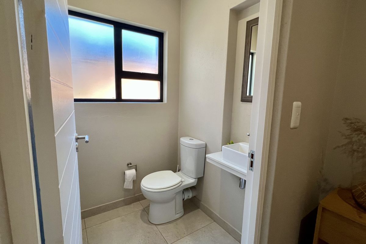 A clean and functional guest bathroom featuring a modern toilet, wall-mounted basin, and neutral tiled flooring with natural light from an obscured window.
