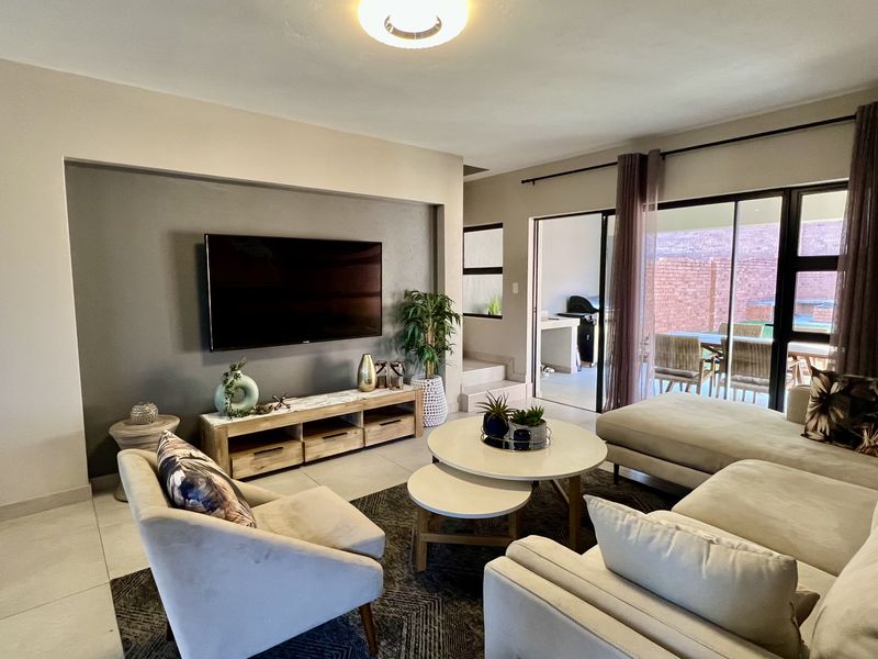 A well-maintained living room featuring a recessed feature wall, tiled flooring, and large sliding glass doors providing access to the outdoor patio area.