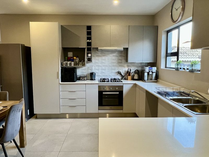 Modern open-plan kitchen featuring sleek cabinetry, stone countertops, integrated gas hob, electric oven, and a double bowl sink, seamlessly flowing into the dining area.