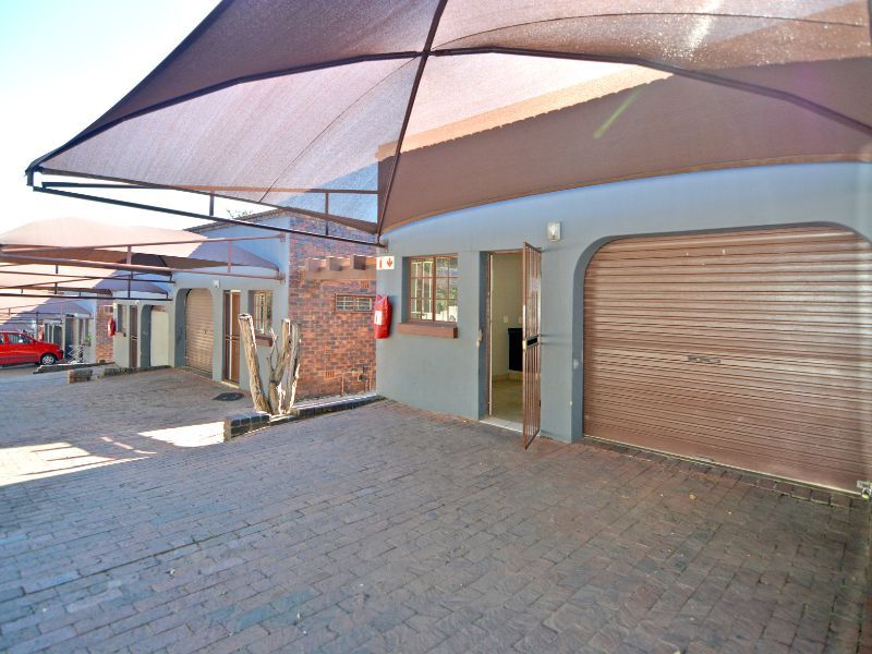 Front exterior view of a townhouse featuring a roller garage door, brick paved driveway, and a protective shade sail structure.