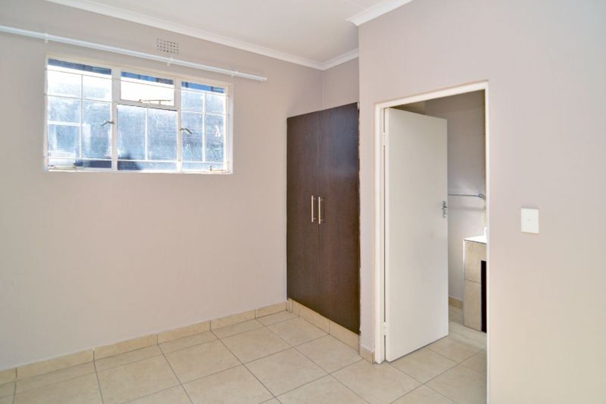A clean, empty bedroom featuring neutral tiled flooring, a built-in cupboard, and direct access to an adjoining bathroom.