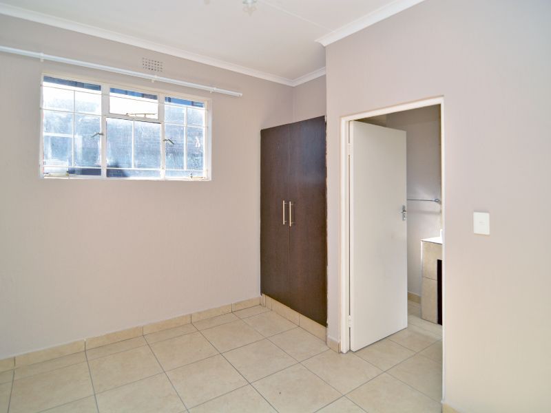A clean, empty bedroom featuring neutral tiled flooring, a built-in cupboard, and direct access to an adjoining bathroom.