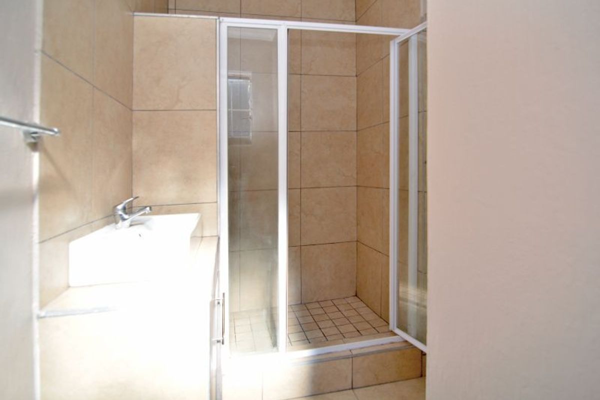 A functional bathroom featuring a tiled shower enclosure, vanity basin with mixer tap, and neutral wall and floor tiling.
