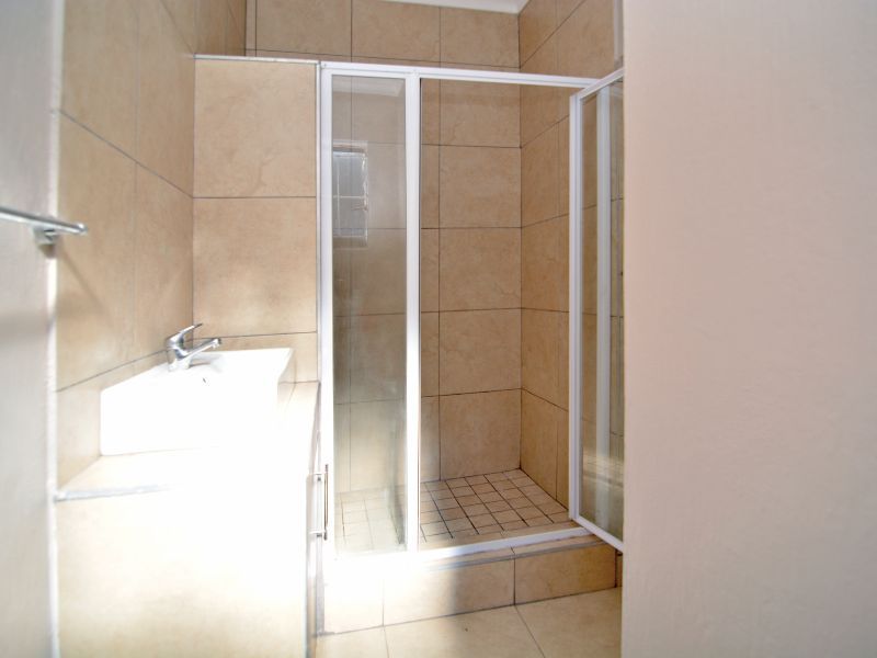 A functional bathroom featuring a tiled shower enclosure, vanity basin with mixer tap, and neutral wall and floor tiling.