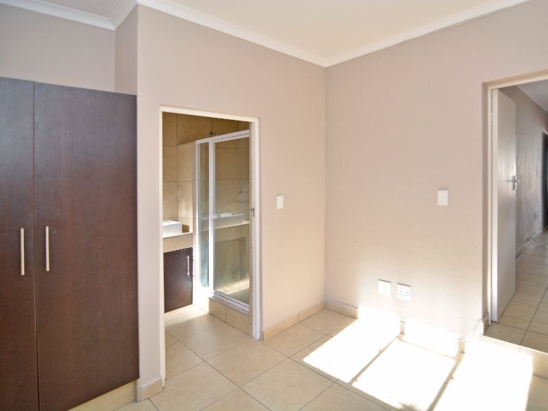 A bright, neutral-toned bedroom featuring tiled flooring, a built-in cupboard, and direct access to an en-suite bathroom with a shower.