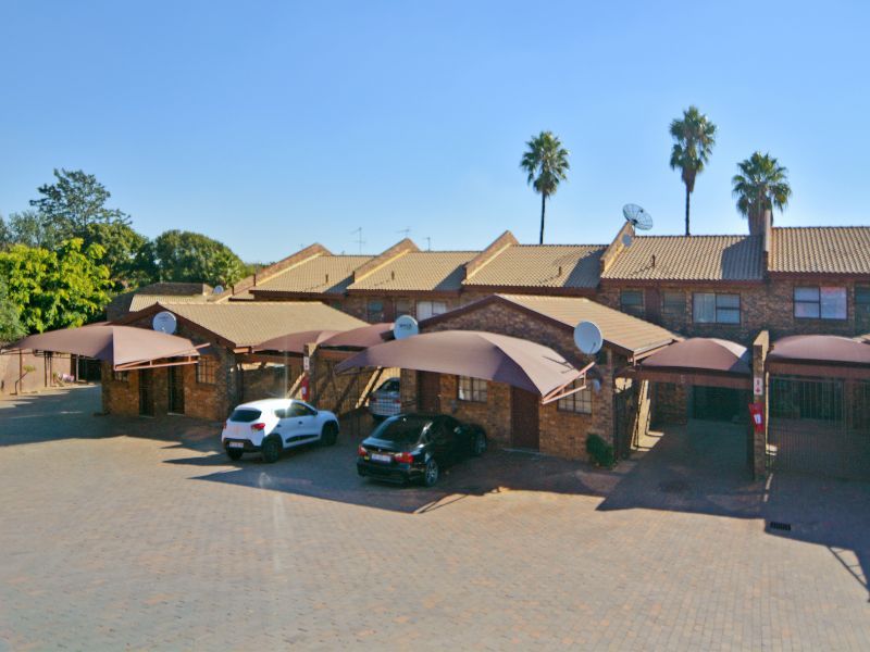 Front elevation of a townhouse complex featuring brick facades, tiled roofing, and dedicated carport parking areas with shade sails.