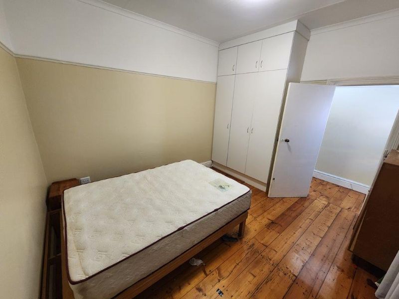 A bedroom featuring original timber flooring, built-in wardrobe storage, and neutral wall finishes.