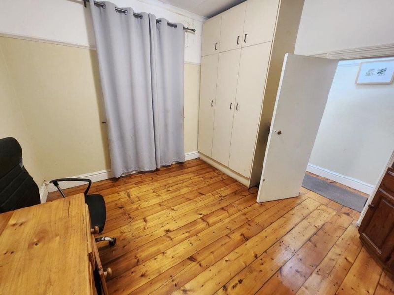 A bedroom featuring original timber flooring, built-in wardrobe storage, and a picture rail, requiring some cosmetic attention to the upper wall and ceiling finishes.