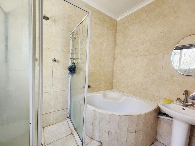 A functional bathroom featuring a corner bathtub, separate shower enclosure, and a pedestal sink with neutral wall and floor tiling.