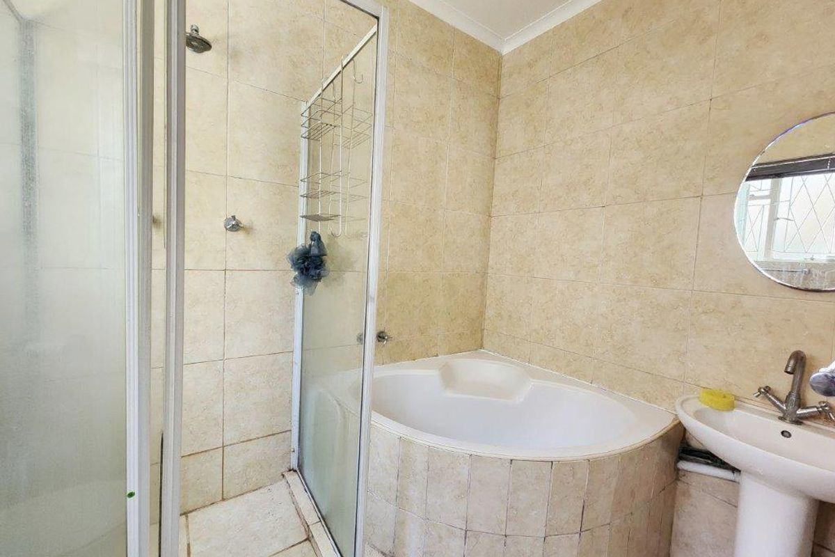 A functional bathroom featuring a corner bathtub, separate shower enclosure, and a pedestal sink with neutral wall and floor tiling.
