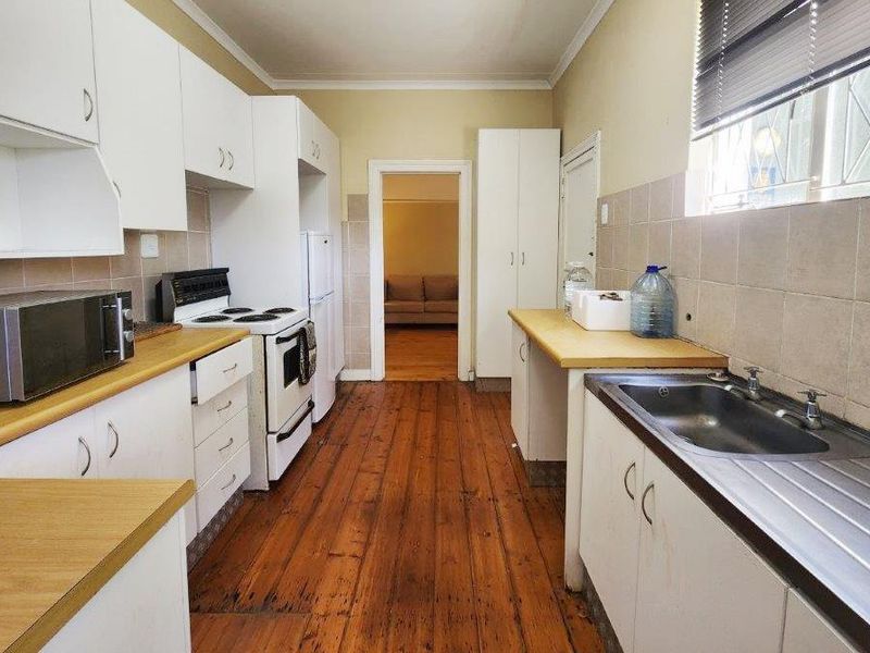 Functional kitchen featuring white cabinetry, laminate countertops, stainless steel sink, and timber flooring, offering a practical layout with potential for modern updates.
