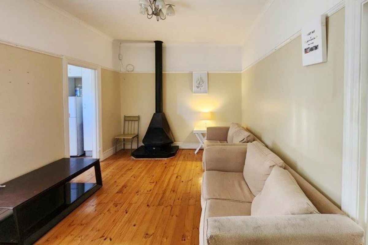 Living room featuring original timber flooring, a central freestanding fireplace, and classic picture rails, offering a cozy and traditional atmosphere.