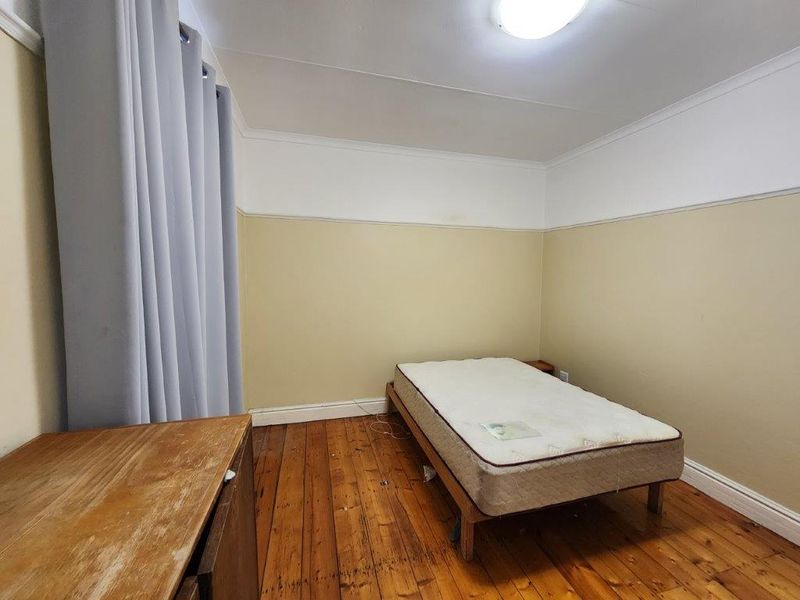 A simple bedroom featuring original hardwood flooring, neutral wall tones, and classic cove cornicing, offering a blank canvas for potential updates.