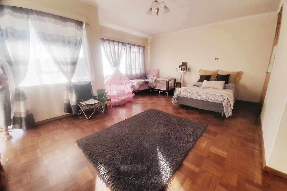 Spacious bedroom featuring classic parquet flooring and built-in storage, offering a versatile layout with ample natural light from large windows.