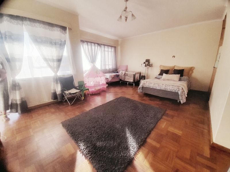 Spacious bedroom featuring classic parquet flooring and built-in storage, offering a versatile layout with ample natural light from large windows.