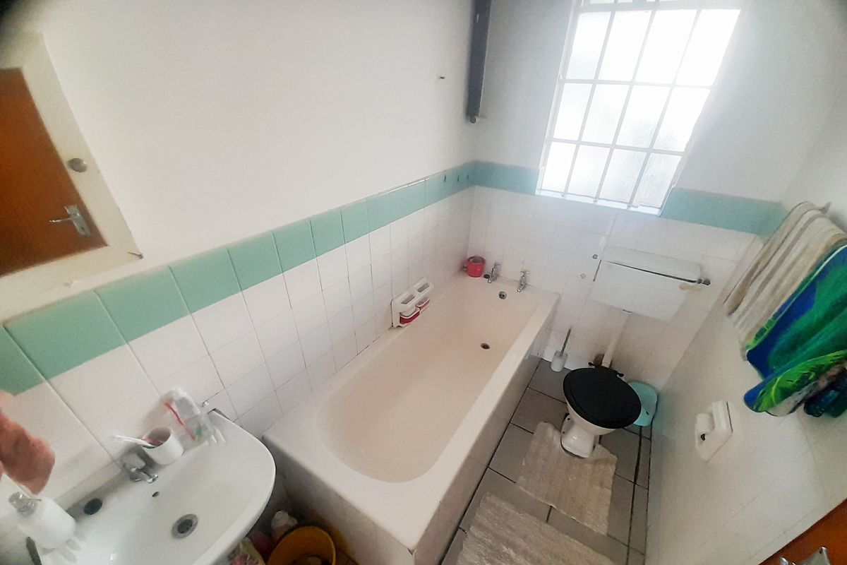 A functional bathroom featuring a bathtub, pedestal basin, and toilet with dated wall tiling and a window with security bars.