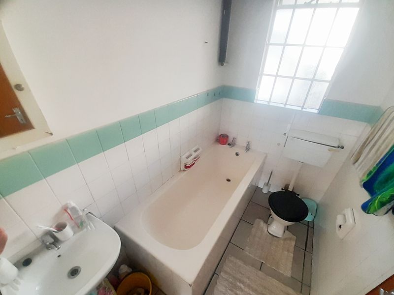 A functional bathroom featuring a bathtub, pedestal basin, and toilet with dated wall tiling and a window with security bars.