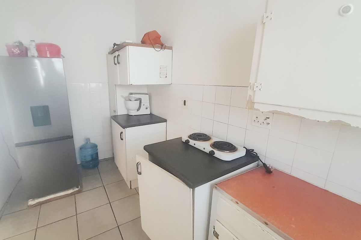 A compact kitchen featuring tiled flooring, a tiled backsplash, laminate countertops, and built-in cabinetry with an electric hob.