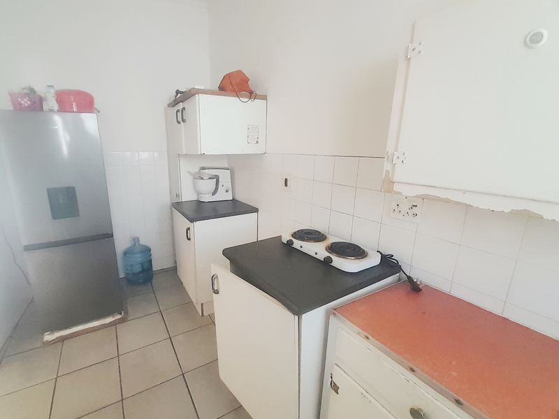 A compact kitchen featuring tiled flooring, a tiled backsplash, laminate countertops, and built-in cabinetry with an electric hob.