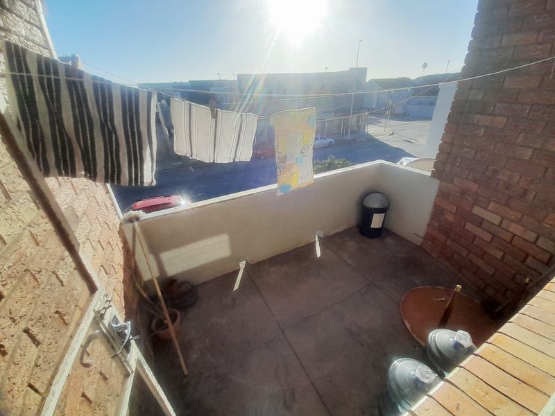 A compact outdoor balcony area featuring brick walls and concrete flooring, offering an open view of the surrounding street.