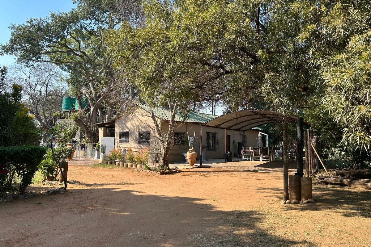 Rear view of the farm dwelling featuring a metal carport, established trees, and a water storage tank set within a natural garden landscape.