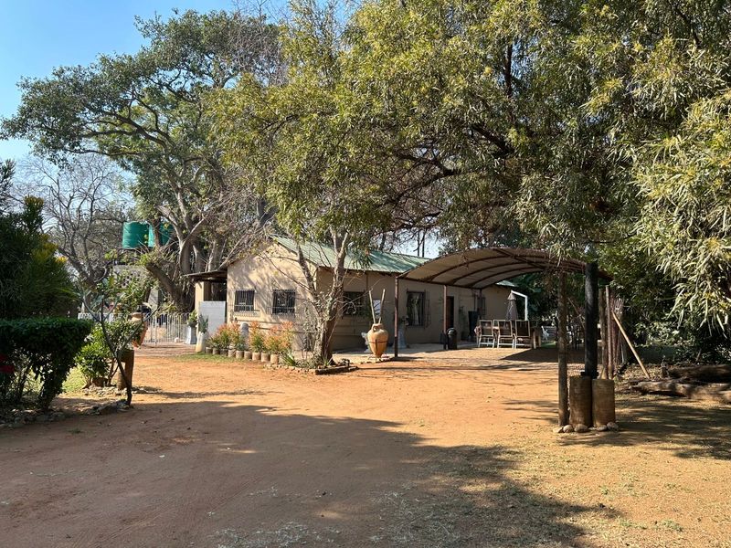 Rear view of the farm dwelling featuring a metal carport, established trees, and a water storage tank set within a natural garden landscape.