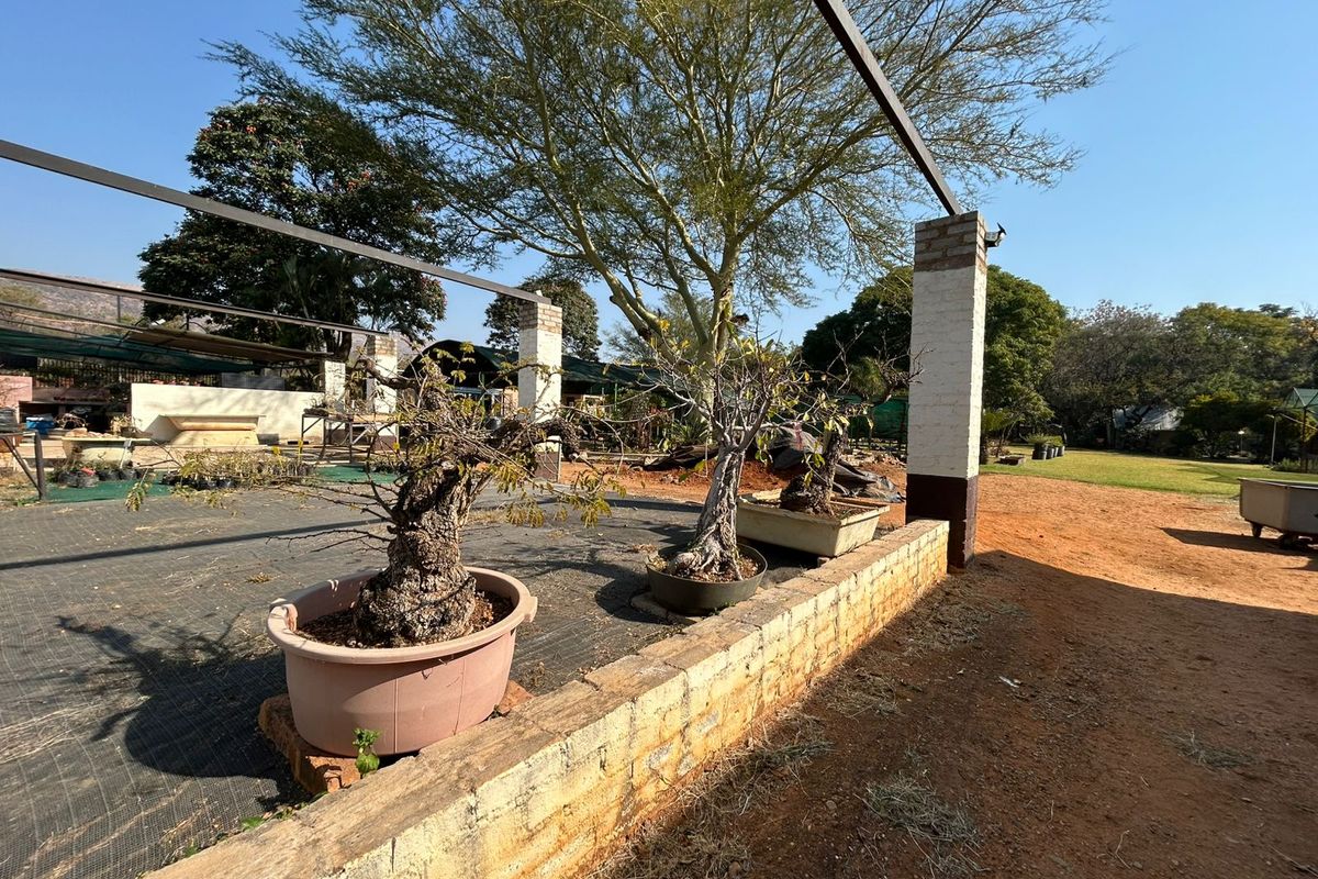 An outdoor garden area featuring a brick retaining wall and a steel pergola structure, set within a spacious farm property landscape.