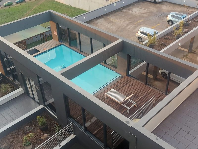 Aerial view of a modern apartment complex pool area featuring a swimming pool, timber decking, and contemporary architectural concrete framing.