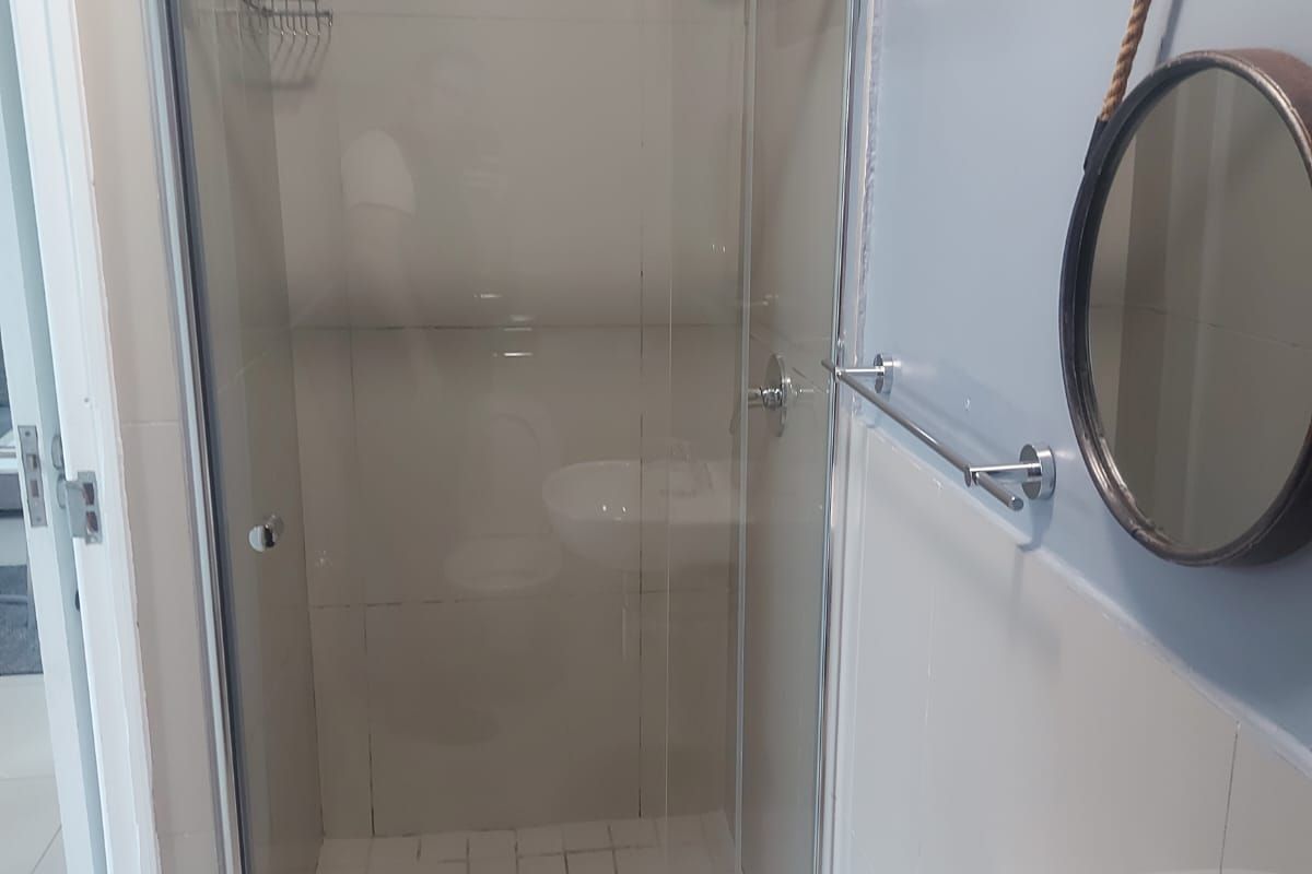 A clean, functional bathroom featuring a glass-enclosed shower, wall-mounted basin with chrome fixtures, and neutral wall and floor tiling.