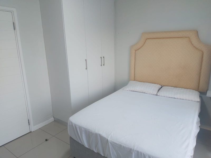 A clean and functional bedroom featuring neutral wall tones, tiled flooring, and a built-in wardrobe for efficient storage.