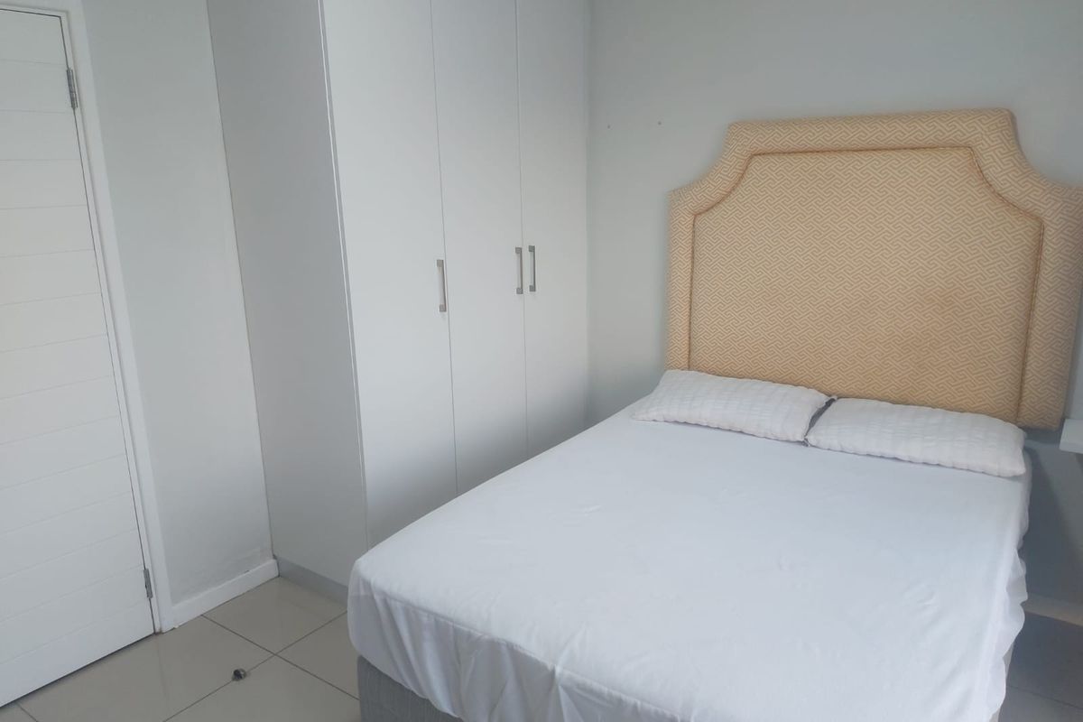 A clean and functional bedroom featuring neutral wall tones, tiled flooring, and a built-in wardrobe for efficient storage.