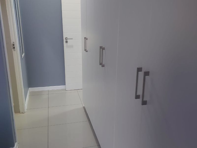 A clean, modern hallway featuring extensive built-in storage cupboards, tiled flooring, and a wall-mounted air conditioning unit.