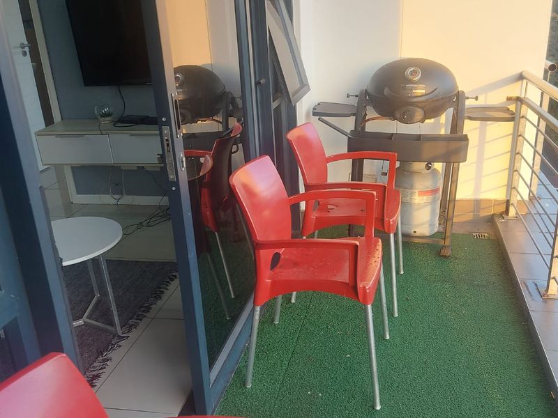 A compact apartment balcony featuring artificial grass flooring, a metal safety railing, and direct access to the living area through a sliding glass door.