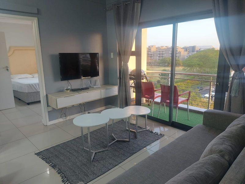 A modern living room featuring tiled floors, a wall-mounted media console, and large sliding glass doors that open onto a balcony with outdoor views.