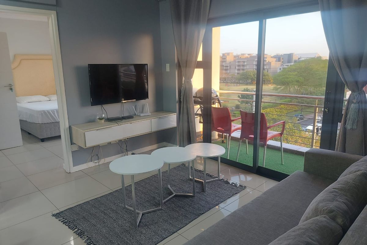 A modern living room featuring tiled floors, a wall-mounted media console, and large sliding glass doors that open onto a balcony with outdoor views.