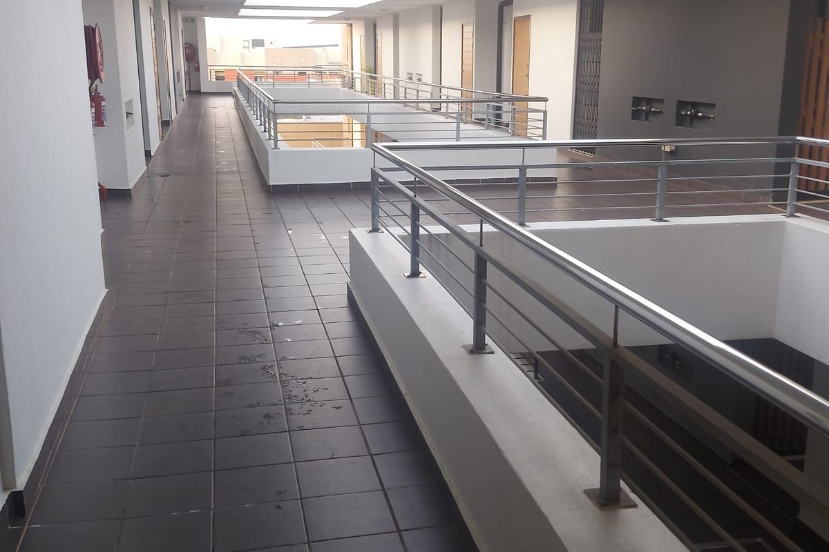 A clean, open-air apartment complex hallway featuring tiled flooring and modern stainless steel balustrades overlooking the central atrium.