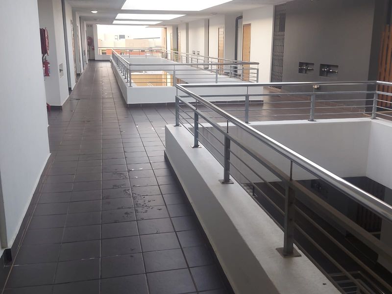 A clean, open-air apartment complex hallway featuring tiled flooring and modern stainless steel balustrades overlooking the central atrium.