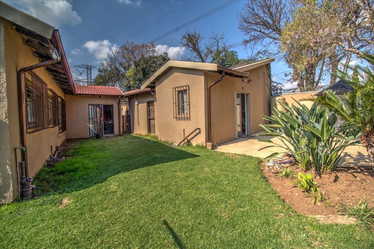 A view of the rear exterior of the house featuring a small lawn, concrete patio area, and security bars on the windows.