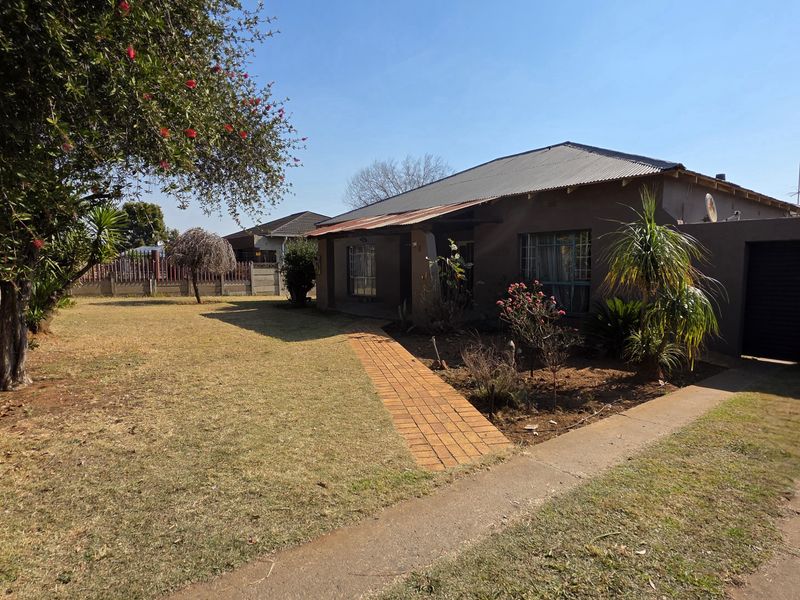 Front exterior view of a single-story house featuring a corrugated metal roof, brick walkway, and attached garage with a spacious front garden.