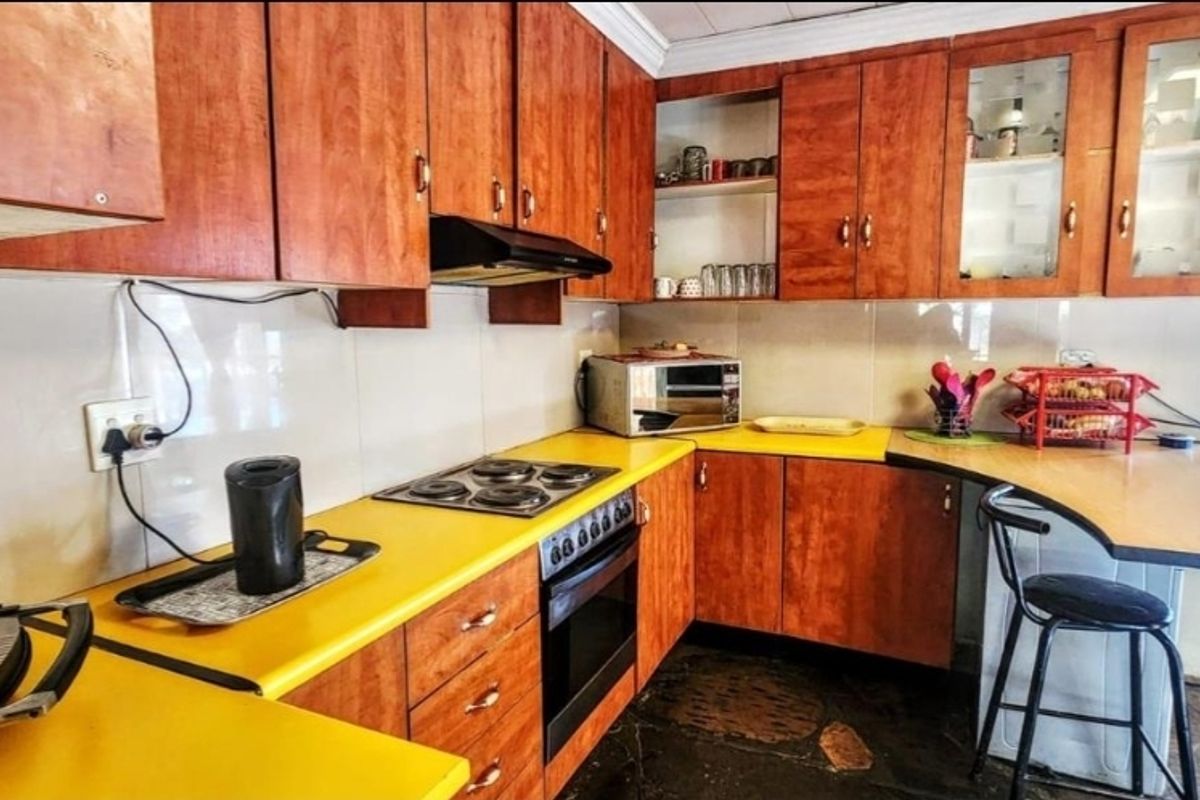 A functional kitchen featuring wood-tone cabinetry, a yellow laminate countertop, built-in oven, and electric hob with an integrated extractor fan.
