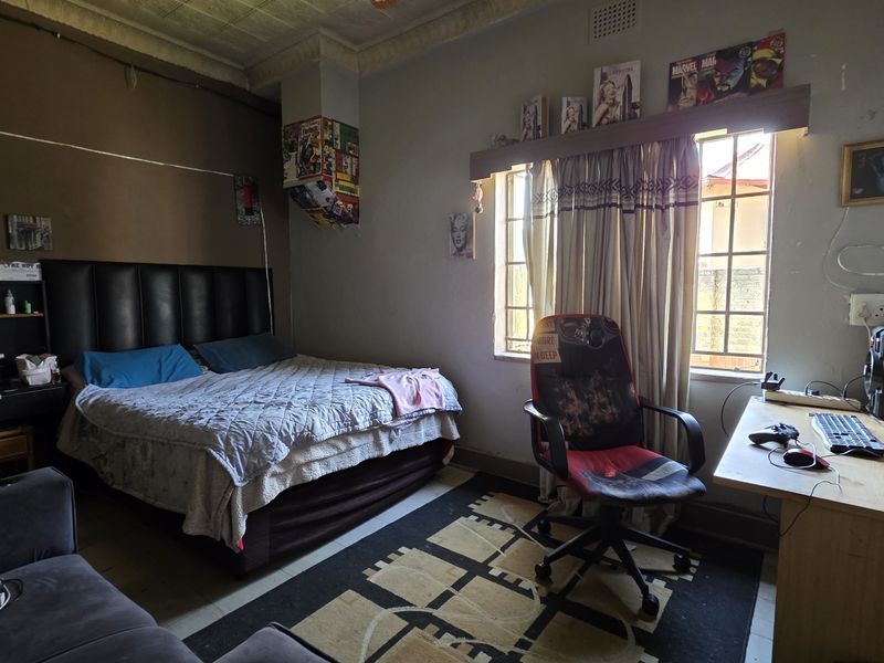 A bedroom featuring tiled flooring, security bars on the windows, and decorative ceiling cornicing, currently showing signs of wear and tear.