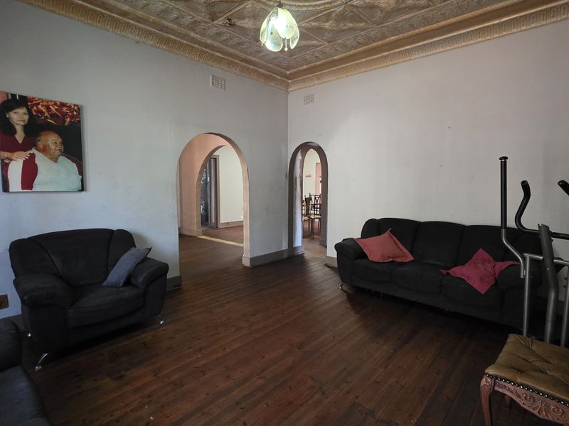 Spacious living room featuring original ornate pressed metal ceilings, polished timber flooring, and classic arched architectural transitions between rooms.