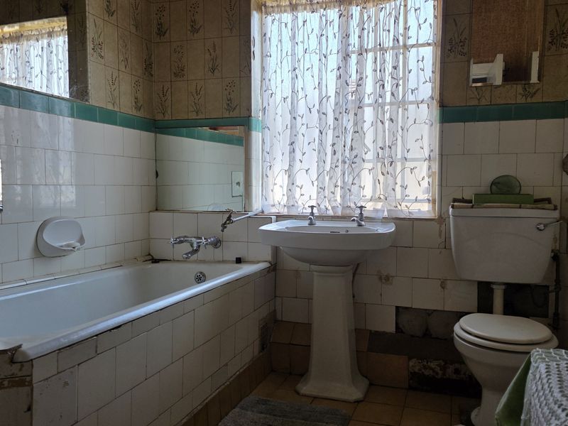 A dated bathroom featuring a pedestal basin, bathtub, and toilet, requiring significant renovation and tile repairs to modernize the space.