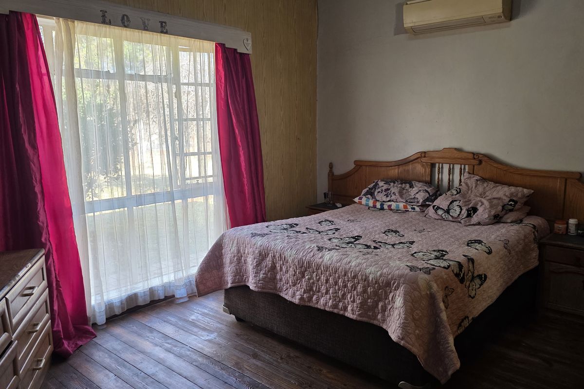 A bedroom featuring timber flooring, a split-system air conditioner, and a large window allowing natural light.