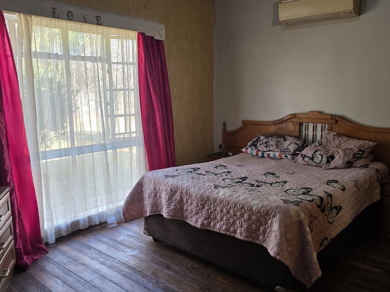 A bedroom featuring timber flooring, a split-system air conditioner, and a large window allowing natural light.