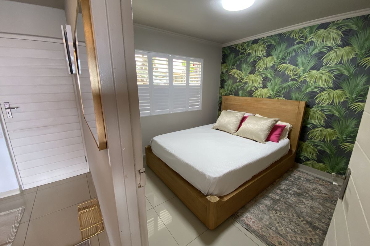 A well-maintained bedroom featuring tiled flooring, plantation shutters, and a bold tropical-themed feature wall.