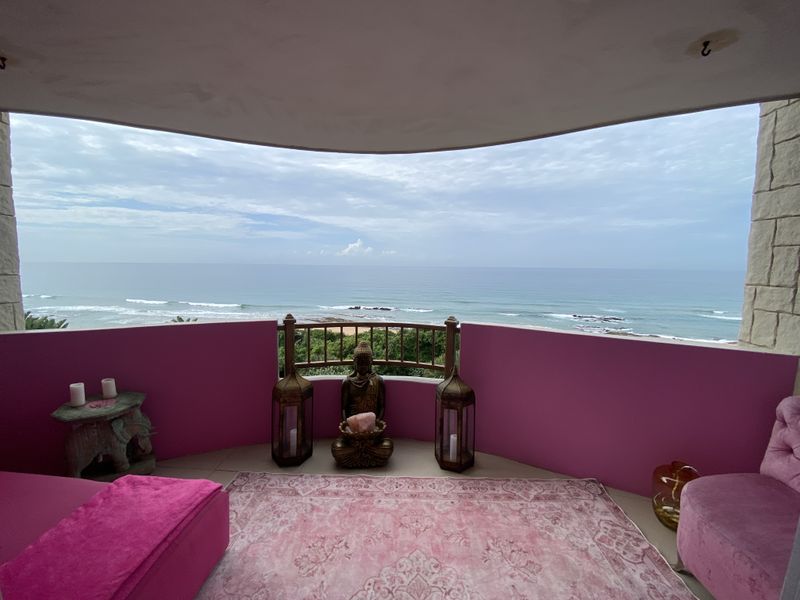 A covered balcony featuring a metal balustrade and stone-clad pillars, offering expansive ocean views and a private outdoor space.